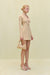 Side view of a woman wearing a cream knit, long sleeve mini dress that features a plunging wood-beaded detail and a keyhole cutout at the bust. 