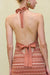 Close up back view of a woman wearing an orange stripe knit midi dress that features a tie up halter neck and a low back with an adjustable tie bow detail on the mid back. 