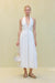 Woman wearing a white poplin midi dress that features a plunging halter neck and wire details at the bust, paired with a white handbag and tank sandals. 