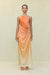 Woman wearing a one shoulder orange ombre gown that features a knot at the hip and ruched draping throughout. 
