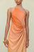 Close up of a woman wearing a one shoulder orange ombre gown that features a knot at the hip and ruched draping throughout. 