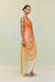 Side view of a woman wearing a one shoulder orange ombre gown that features a knot at the hip and ruched draping throughout. 