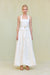 Woman wearing a white cropped halter top with a square neckline and an adjustable bow in the front, paired with a white maxi skirt. 