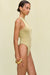 Side view of a woman wearing a metallic gold knit bodysuit that features a high neck and high cut leg, paired with a gold bangle. 