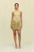 Woman wearing a gold knit mini skirt with a plunging waistline that is adorned with all over gold knit fringe, paired with a gold bodysuit and gold accessories. 