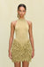 Close up of a woman wearing a gold knit mini skirt with a plunging waistline that features all over gold knit fringe, paired with a gold bodysuit. 