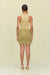 Back view of a woman wearing a gold knit mini skirt that features all over gold knit fringe, paired with a gold bodysuit and gold heels. 