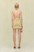 Back view of a woman wearing a gold knit mini dress that features a high neckline and a low back detail with a strap across, paired with gold accessories. 