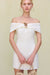 Close up of a woman wearing a white linen mini dress that features an off the shoulder neckline and gold hardware detailing at the bust.