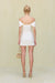 Back view of a woman wearing a white linen mini dress that features an off the shoulder neckline. 