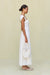 Side view of a woman wearing a white maxi poplin dress that features a sweetheart neck, cap sleeves, and a cutout at the bust, paired with white sandals. 
