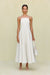 Woman wearing a white maxi dress that features a square neck with gold-toned grommet details attaching the spaghetti straps and a full skirt. 
