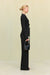 Side view of a woman wearing a black, collared, long sleeve shirt that features two grommet-tie details in the front, paired with black pants. 
