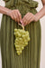 Woman holding a light green acrylic clutch that resembles a bunch of grapes with a gold toned stem. 