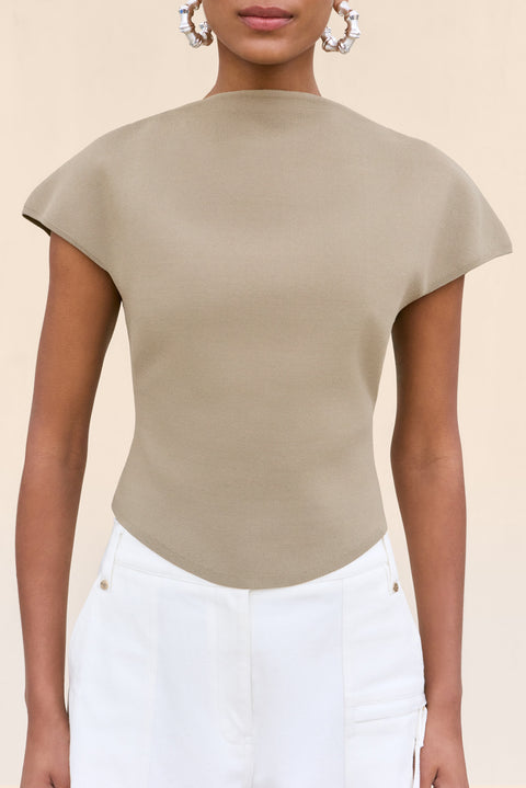 Close up of a woman wearing a tan knit shirt that features a mock neck and structures cap sleeves, paired with white cargo pants.
