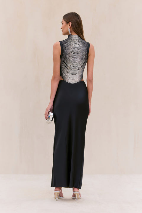 Back-facing woman wearing a black silk maxi skirt paired with a tank top that features black and silver ombre beaded strings draping across the bodice. 
