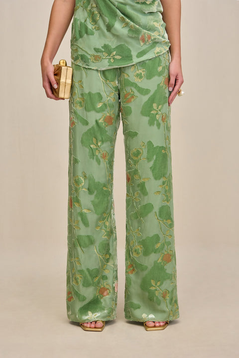Close up of a woman wearing a green wide leg pant with velvet and silk burnout patterns and gold details, paired with a matching top.