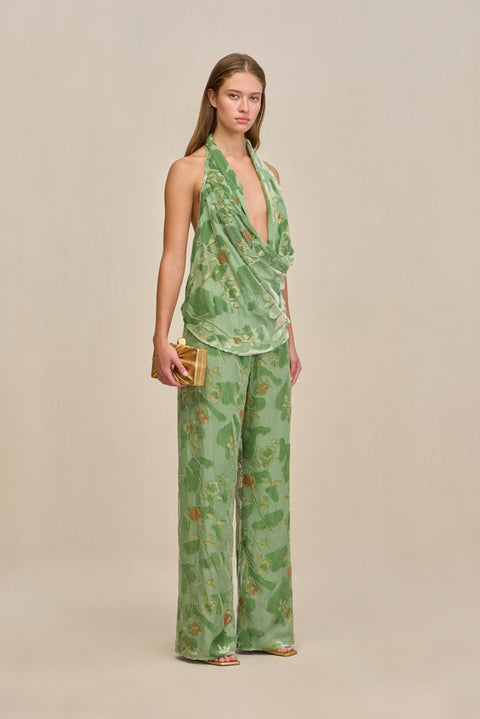 Side-facing woman wearing a green wide leg pant with velvet and silk burnout patterns and gold details, paired with a matching top.