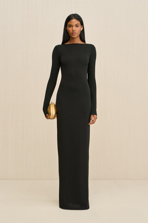 Woman wearing a black long-sleeve gown holding a gold clutch against a beige background