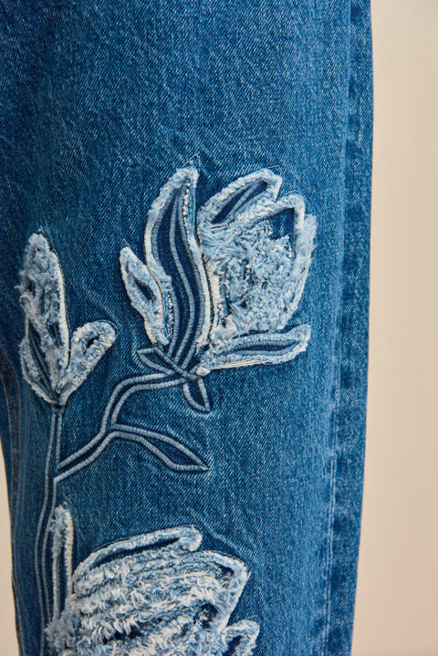 Detail shot of the distressed floral embroidery on a pair of blue wide leg jeans. 