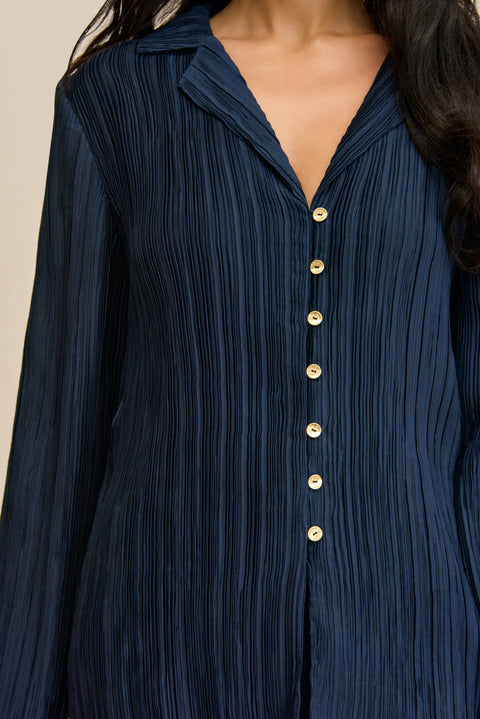 Close up of a woman wearing a navy plisse button down shirt that features pearlescent contrast buttons. 