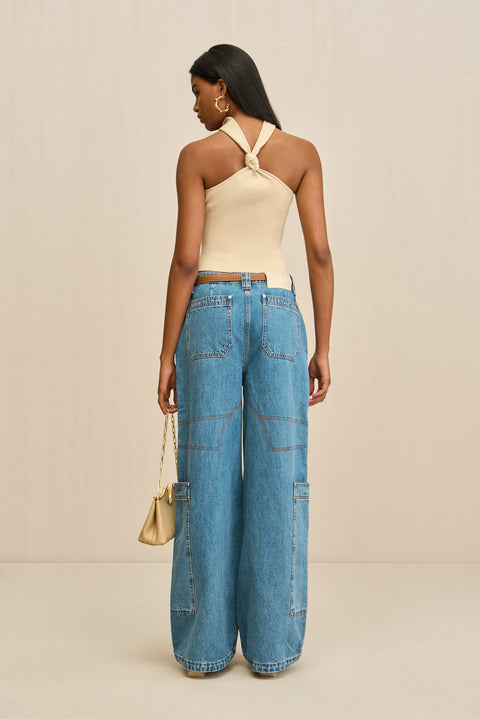 Back-facing woman wearing a tan knit top that has a choker detail with a chic knot detail in the back, paired with blue wide leg jeans. 