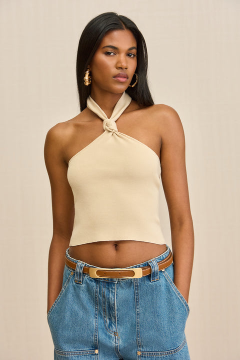 Close up of a woman wearing a tan, knit halter top with a knot detail at the neck. 