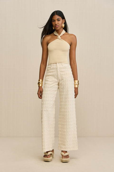 Woman wearing a tan knit halter top with a knot detail at the neck, paired with cream pants. 