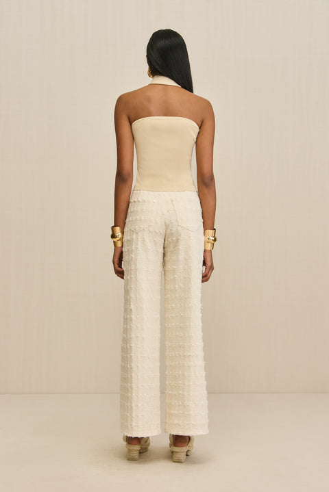 Back-facing woman wearing a tan, knit halter top with cream wide leg pants. 