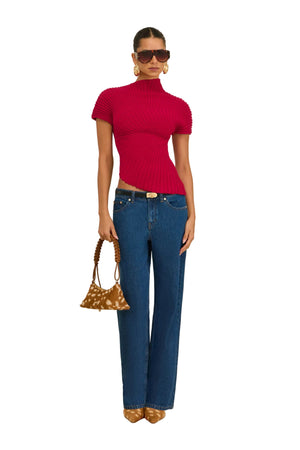 Woman wearing a red top and blue jeans, holding a patterned handbag on a beige background