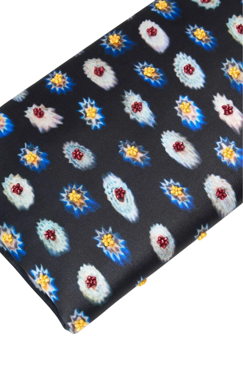 A close-up of a black fabric product, a clutch, featuring a repeating pattern of stylized floral motifs in blue, white, yellow, and red.