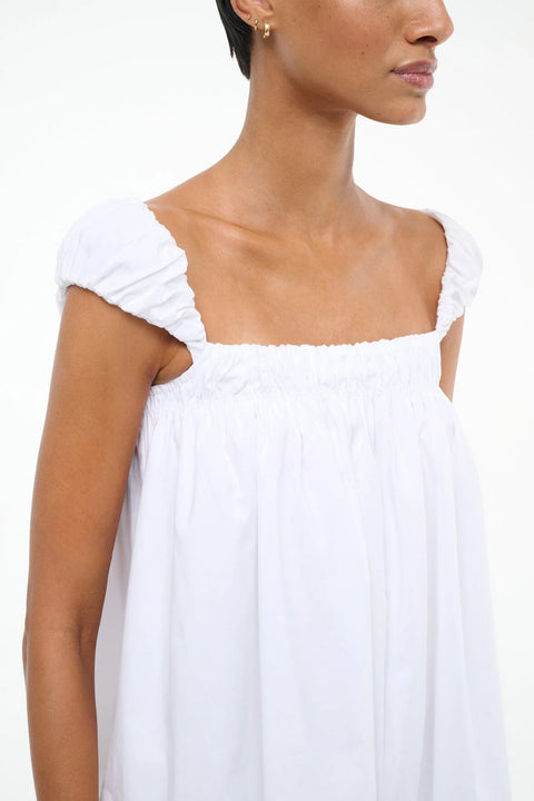 Close up of a woman wearing a white mini babydoll dress that features a ruched band across the chest and puffed cap sleeves. 