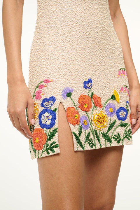 Detail shot of the intricate, colorful floral beading along the hem of a ream beaded mini dress, featuring a side slit. 