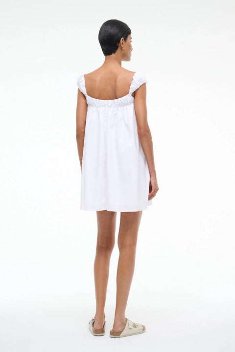 Back view of a woman wearing a white mini babydoll dress that features puffed cap sleeves. 
