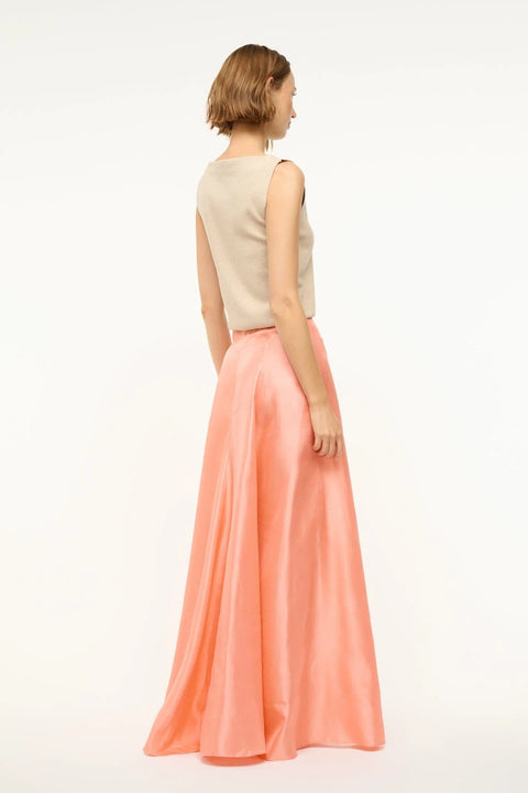 Back view of a woman wearing a pink silk, Aline, maxi skirt that features a back zipper and sits at the natural waist, paired with a tan sweater vest. 