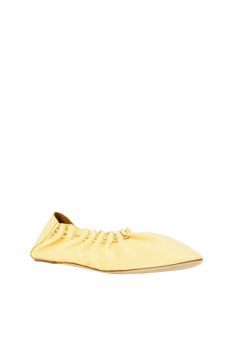 A single pale yellow pointed-toe flat shoe with gathered detailing and decorative laces, shown from a side profile on a plain white background.