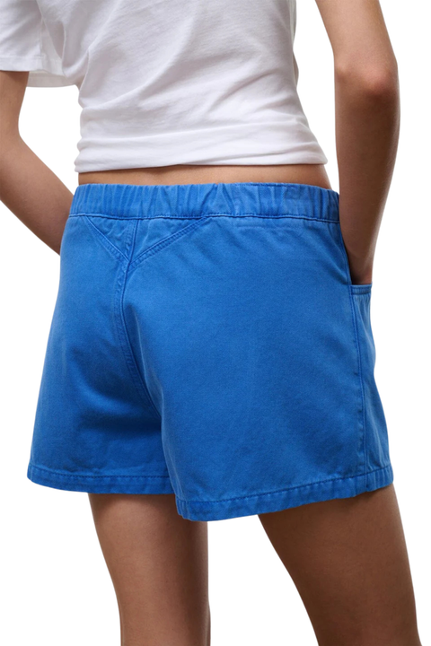 A person wearing bright blue shorts with a white cropped T-shirt, shown from the back against a plain white background.