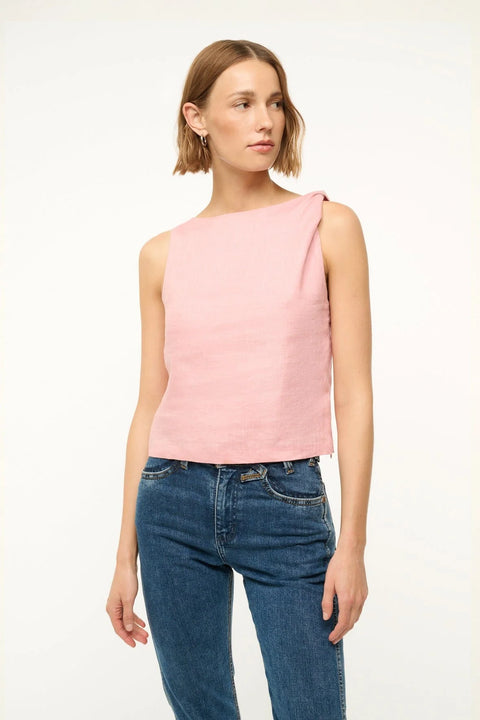 Close up of a woman wearing a pink linen shirt that features a boat neck and a twist detail at the shoulder, paired with jeans. 
