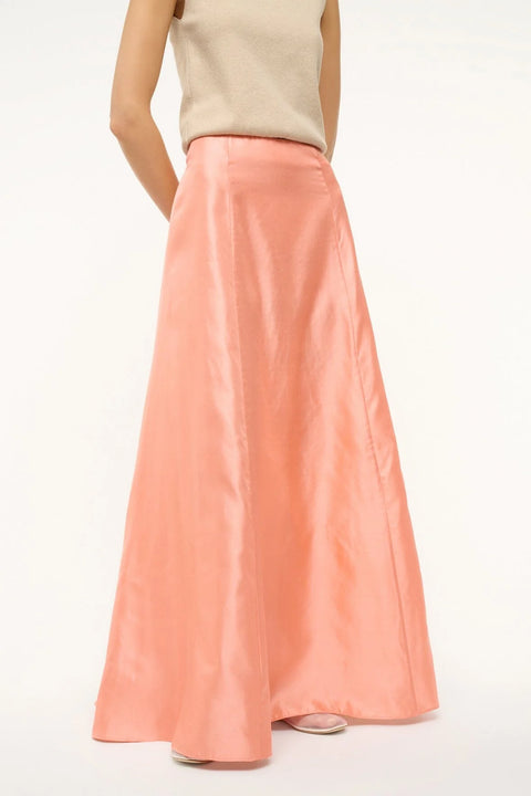 Close up of a woman wearing a pink silk, Aline, maxi skirt that features a back zipper and sits at the natural waist, paired with a tan sweater vest. 