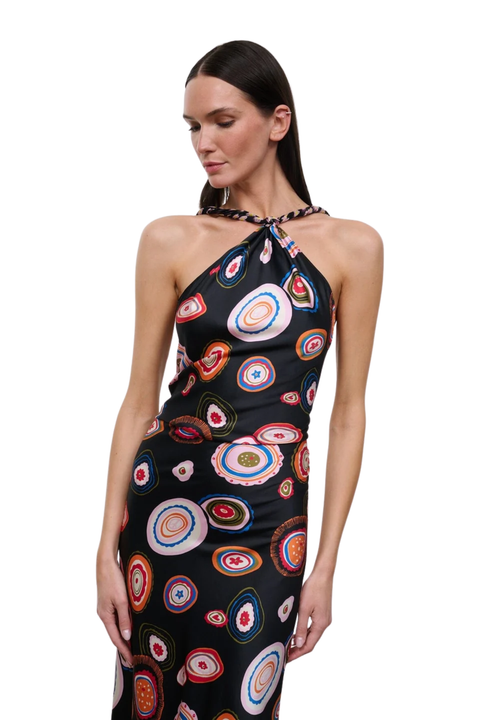 A woman modeling a sleeveless halter-neck dress with a black base and a colorful circular concentric pattern, set against a plain white background.