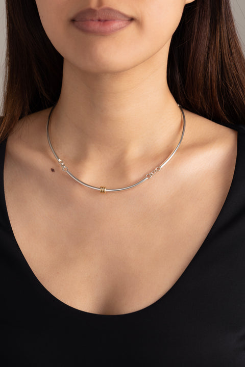 Woman wearing a sterling silver necklace that features three arced bar chained together, one with three yellow gold annulets. 