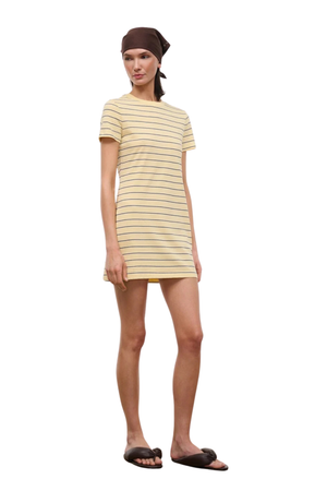 A woman modeling a short-sleeve t-shirt dress with thin horizontal yellow stripes on a cream base, paired with a dark brown headscarf and dark brown slide sandals, set against a plain white background.