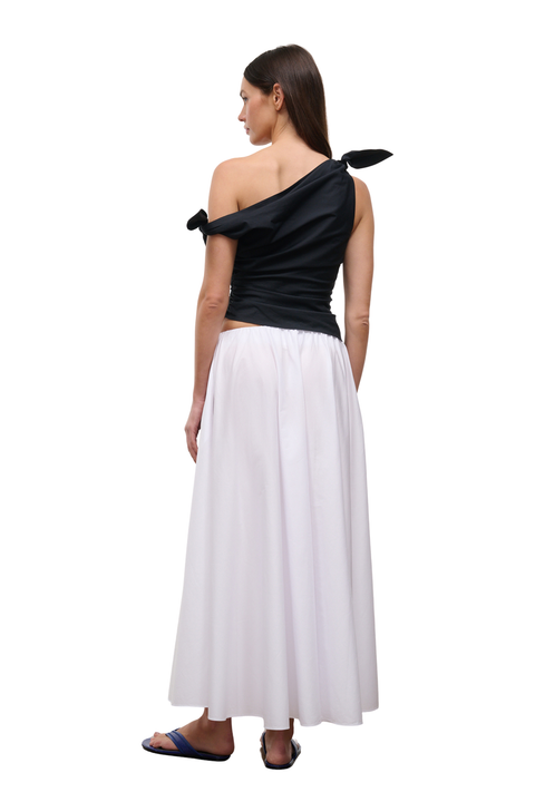 A woman shown from the back wearing a black one-shoulder wrap top with a side tie and a long white skirt, standing against a plain white background.