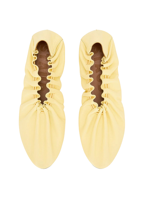 A pair of pale yellow leather slip-on shoes with gathered ruffled detailing around the opening, shown from a top-down view on a white background.