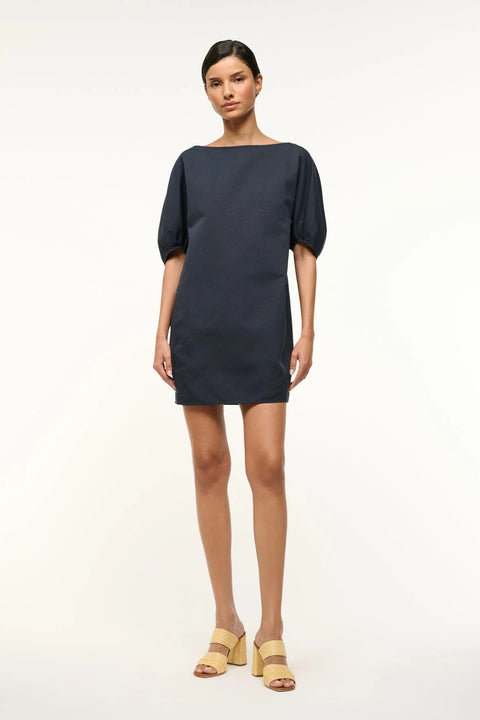 Woman wearing a navy, mini shift dress that features a boat neck and balloon half-sleeves, paired with tan heels. 