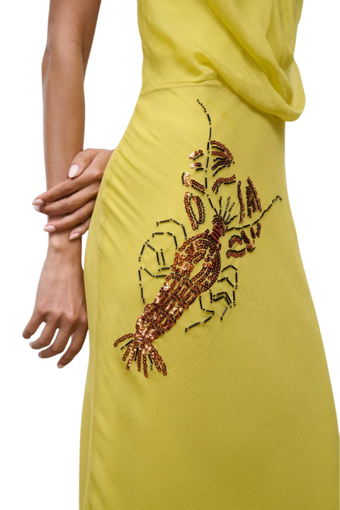 A close-up of a yellow dress featuring a large, detailed lobster applique embellished with brown and gold sequins on the side, worn by a model.
