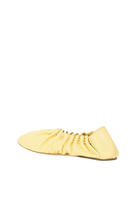 A pale yellow leather slip-on shoe with gathered detailing and decorative eyelets, shown from a side profile on a solid white background.