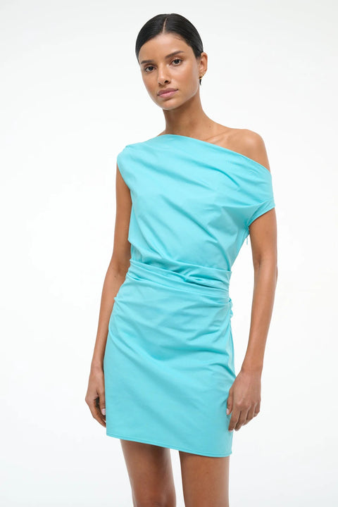 Close up of a Woman wearing a teal mini dress that features an asymmetrical neckline and ruching throughout. 
