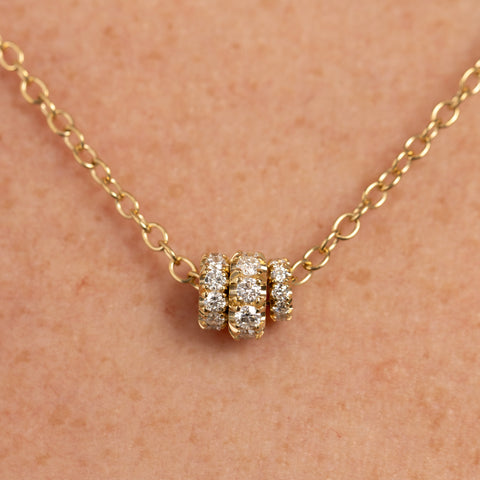 Close up of a woman wearing a yellow gold chain necklace that features three yellow gold annulets of differing size, all pave with diamonds. 