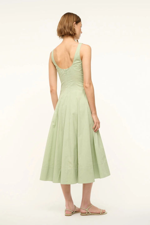 Back view of a woman wearing a sleeveless light green midi dress that features a square neck and corset-style paneling. 